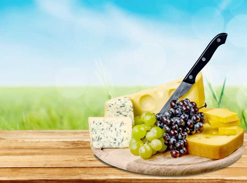 天空背景下木盘中的奶酪水果及刀具