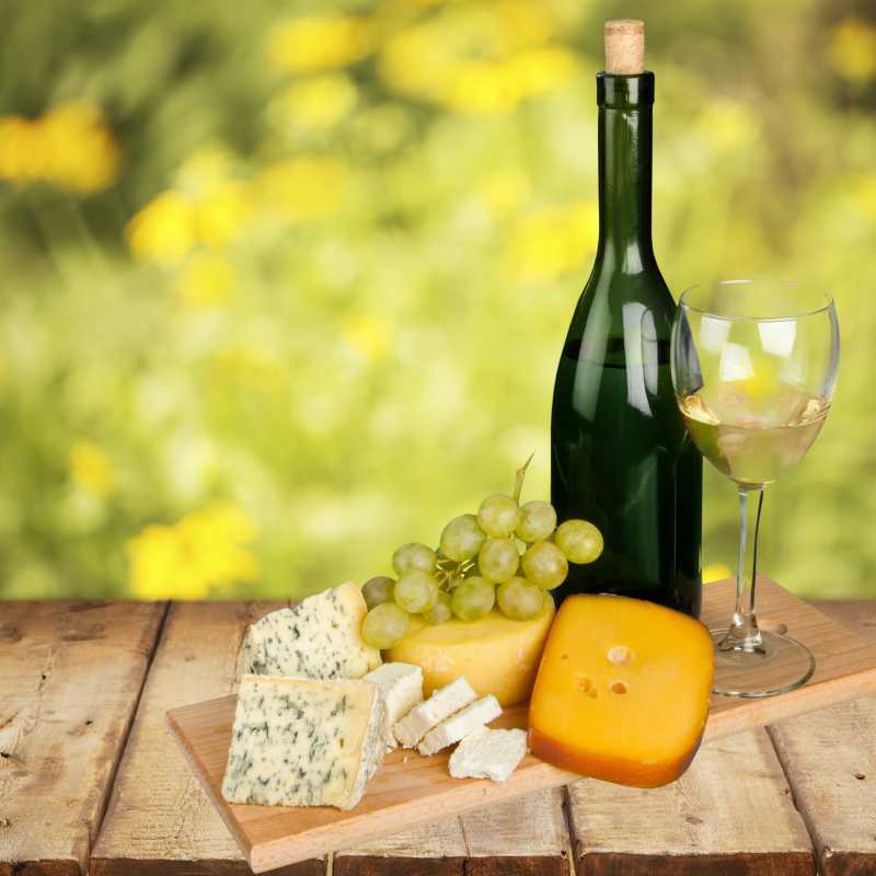 黄色背景的木板上放有奶酪葡萄和酒
