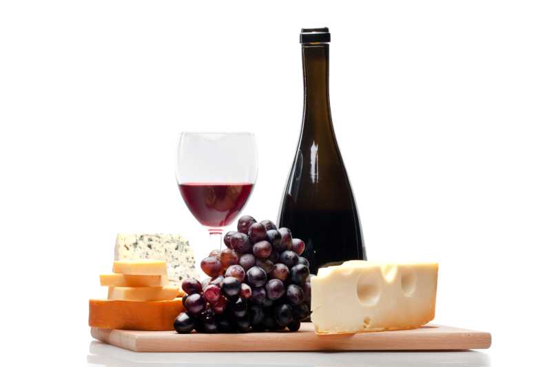 白色背景的木板上放有各种干奶酪以及红酒