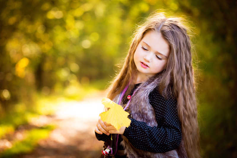 森林里可爱的小女孩拿着一个黄色叶子