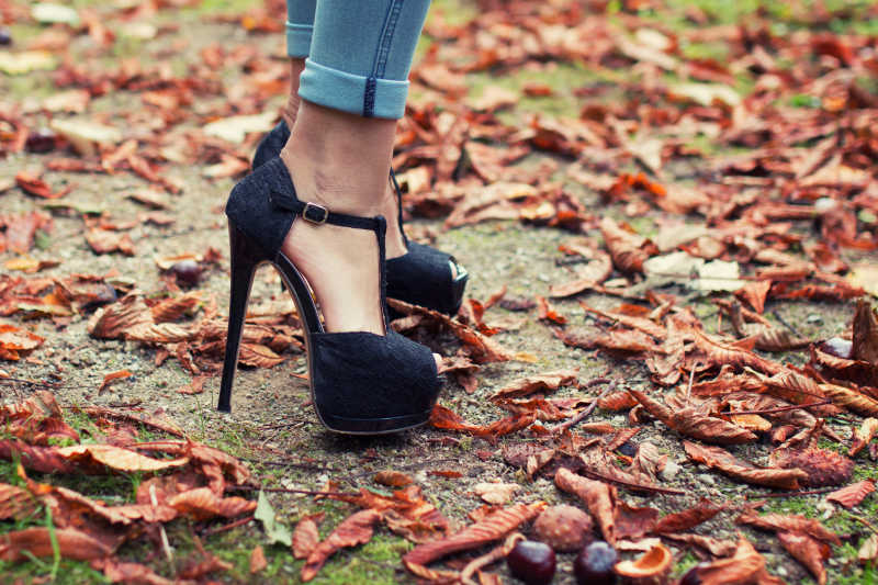 美女穿着黑色高跟鞋站在落叶上特写