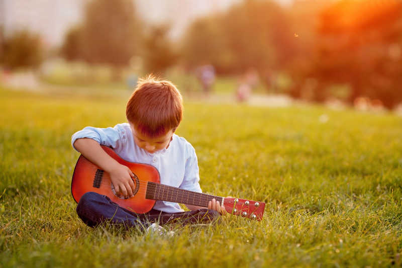 坐在草地上的小男孩弹吉他