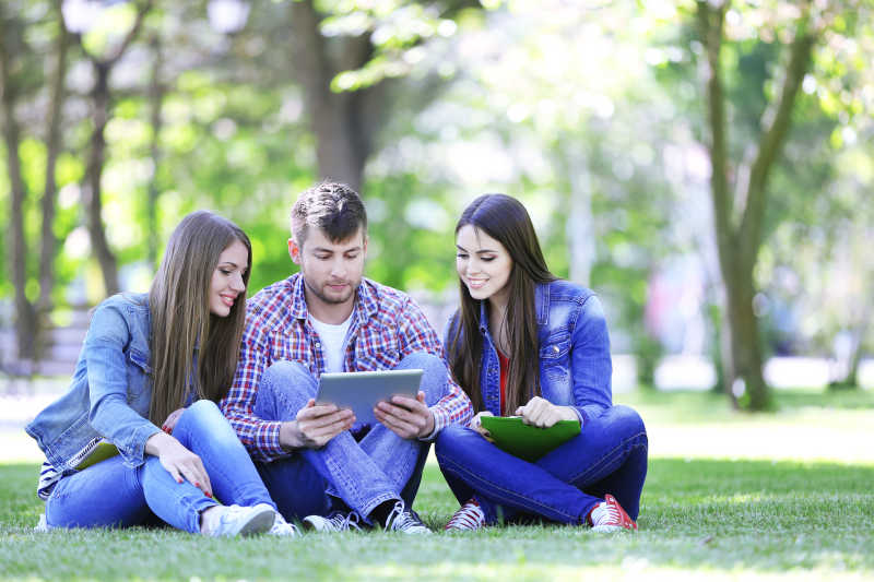 坐在草坪上看着平板电脑的三个年轻人