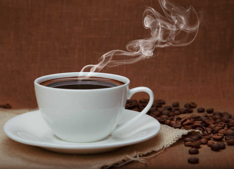 亚麻布上的一杯热咖啡和散落的咖啡豆