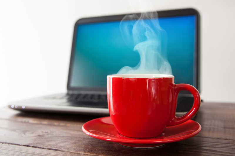 桌子上的红色咖啡杯里的热饮和电脑