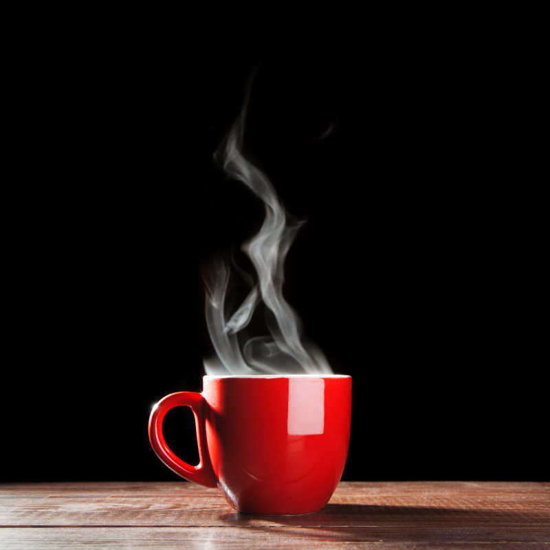 黑色背景下木质桌上的一杯红色杯子盛好的热咖啡