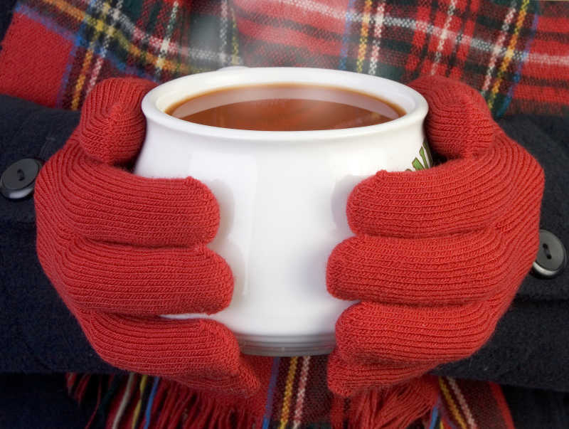 带着红手套的手捧着一杯热气腾腾的番茄汤