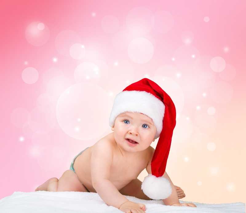 粉色背景上的戴着圣诞帽的可爱婴儿