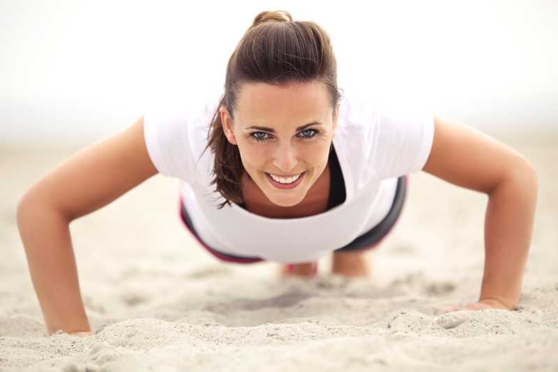 沙滩上微笑着做俯卧撑运动的女子