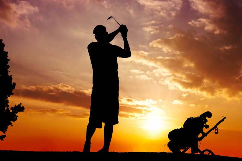 夕阳晚霞上的打高尔夫球人的剪影