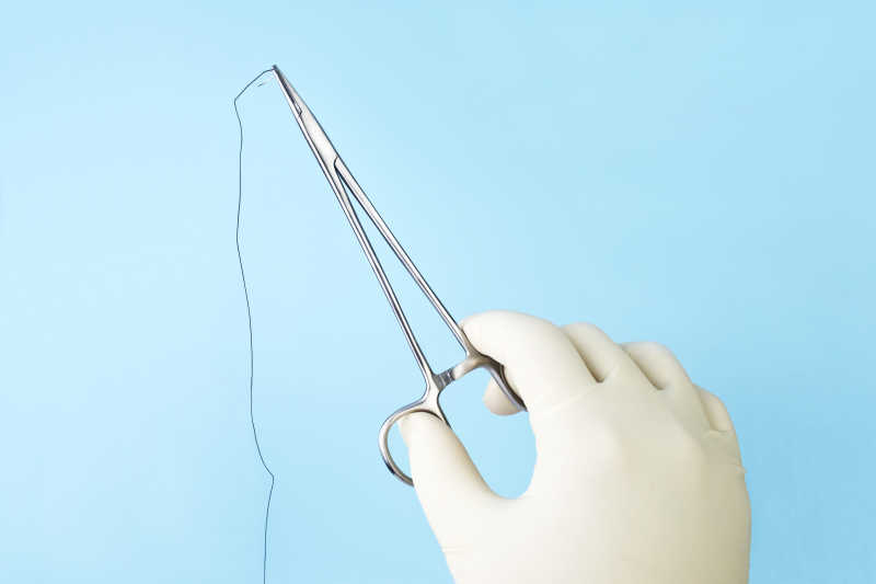 外科医师手拿蓝色丝线缝合手术夹持器