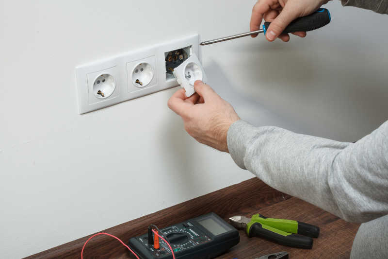 电工拿着螺丝刀在白色墙面上安装插线板