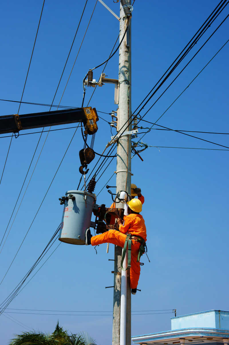 蓝天背景下电工爬到电线杆上修理电线