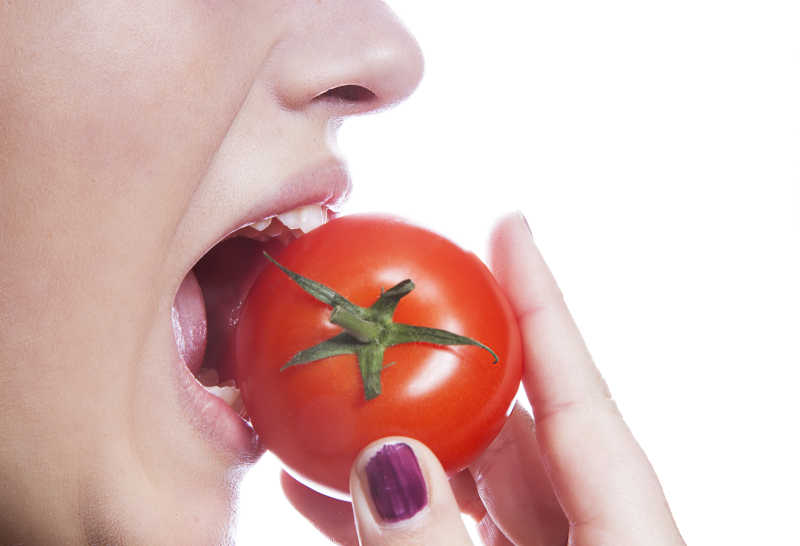 白色背景下吃西红柿的年轻女子