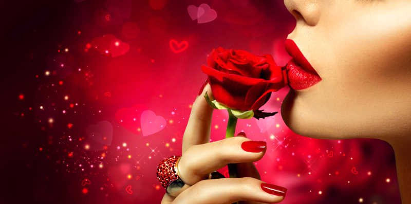 红色情人节背景下有性感红唇的美女模特亲吻红玫瑰花