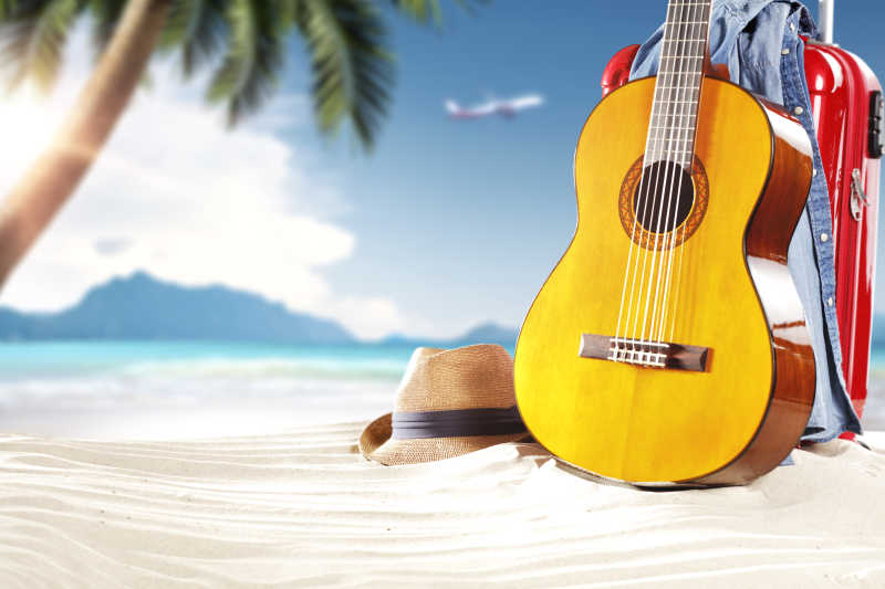 夏季沙滩上的吉他手提箱和帽子