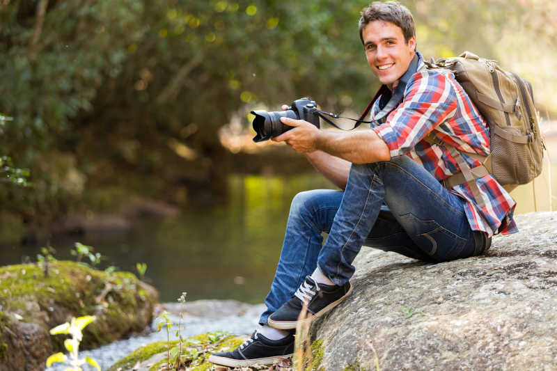 坐在山谷岩石上的拿着单反的年轻摄影师