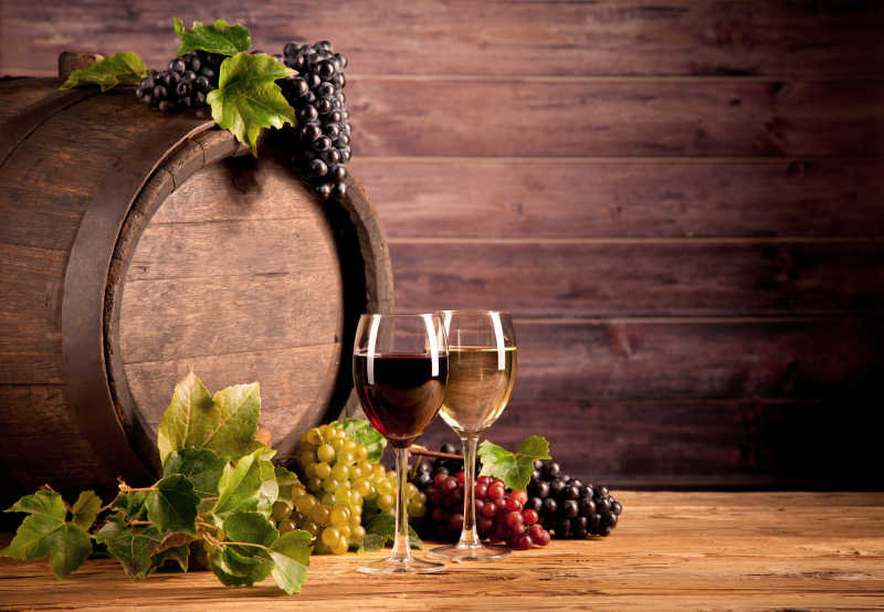 放在木桶旁边的葡萄和玻璃杯里的葡萄酒特写