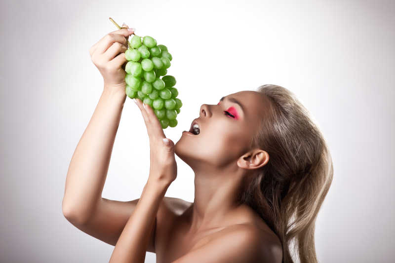 漂亮的年轻女子吃绿色葡萄