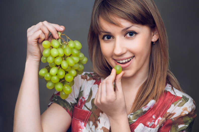 漂亮的女孩正在吃绿色的葡萄