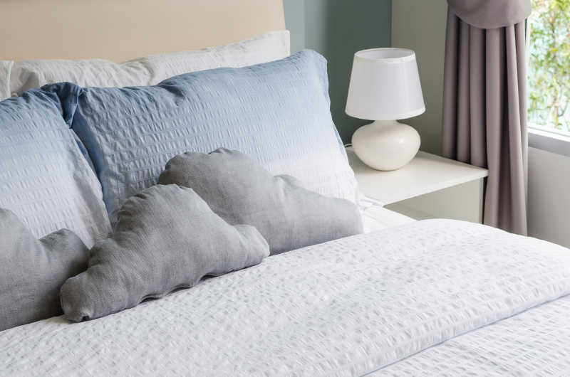灰白色枕头抱枕白色被子和白色床头柜台灯