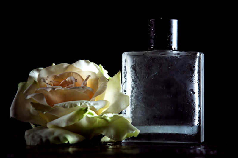 黑色背景上的一朵玫瑰花和香水