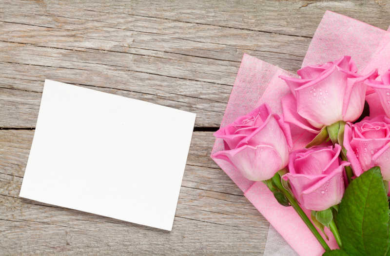 木桌上的粉红玫瑰花束和空白纸条