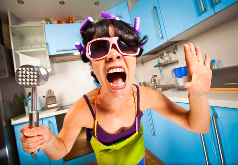 厨房背景下疯狂的主妇拿着烹饪工具尖叫