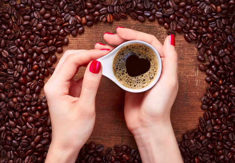 女人握着一杯咖啡手放在咖啡豆中间