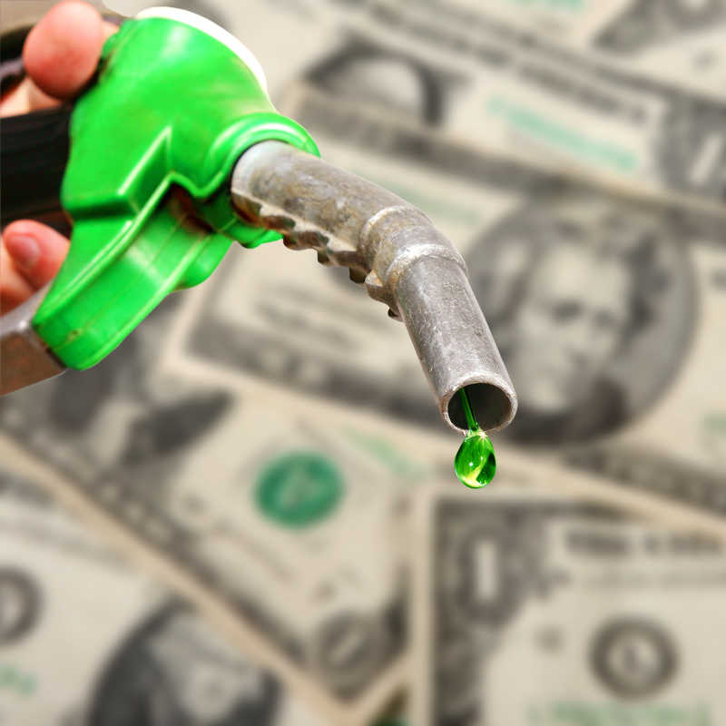 美元纸币背景下的加油枪滴着绿色燃料