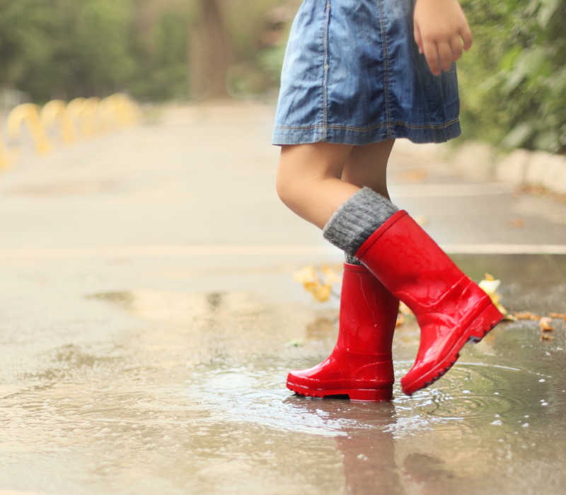 穿着红色雨靴踩在水坑里的小女孩