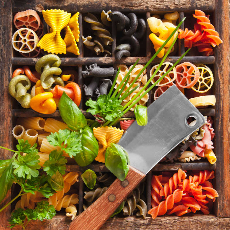 放满各种意大利面的木箱上面放着一把刀和蔬菜