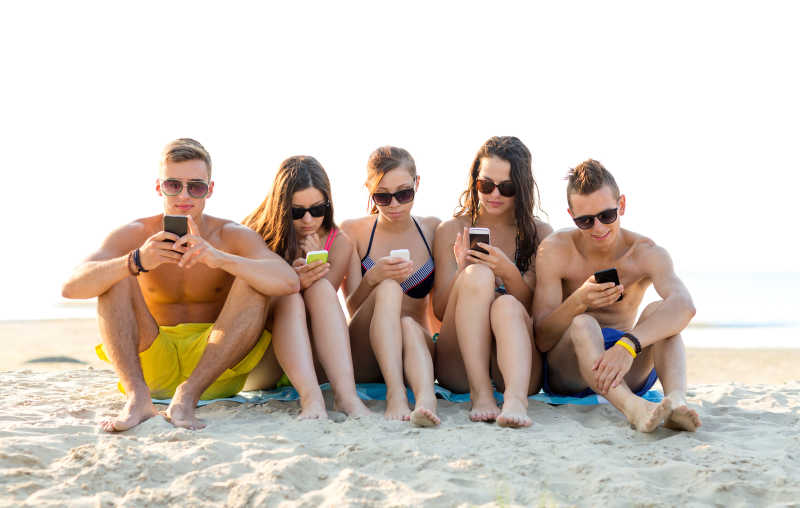 在户外沙滩上低头玩手机的男女