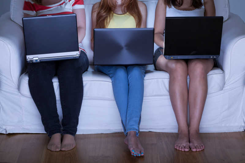 三个坐在沙发上沉迷于电脑的女人