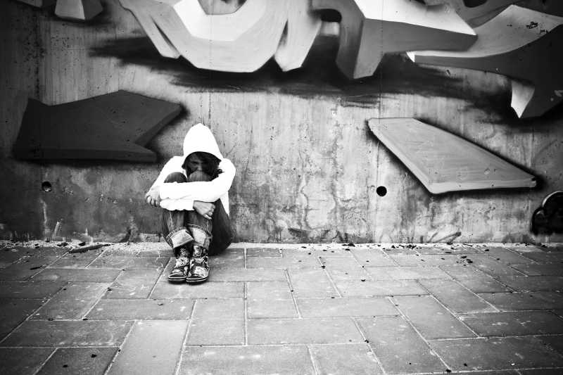 灰色城市墙面涂鸦背景下白衣服少女抱膝坐在地上