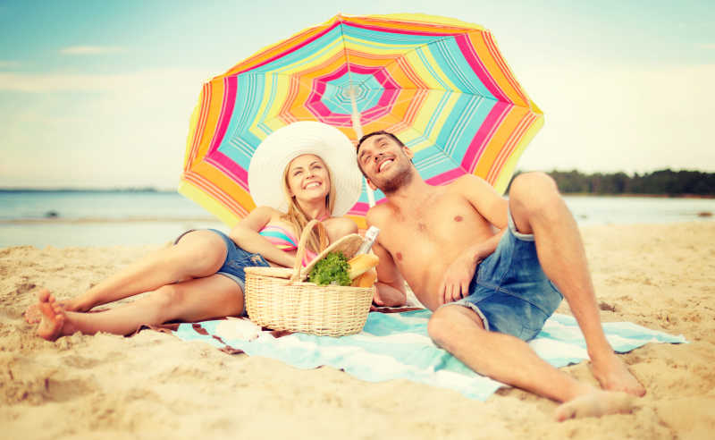 微笑的情侣躺在沙滩雨伞下享受日光浴