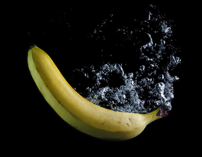 香蕉落在黑色的背景水中引起的气泡抓拍