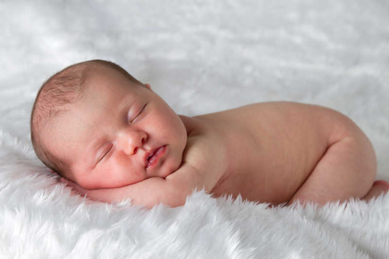 趴在白色毛毯上睡着的新生婴儿