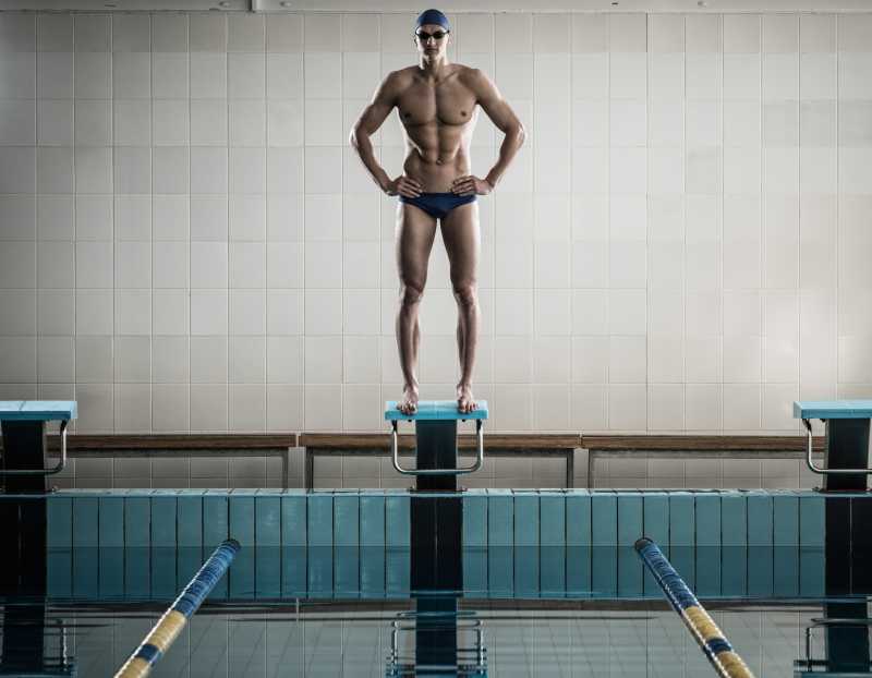 站在游泳池的起跑器上的年轻肌肉游泳运动员