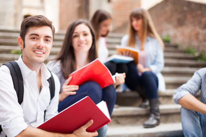 坐在楼梯上的男女大学生手拿红色课本