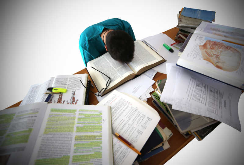 趴在书桌上睡觉的大学生身前有很多书