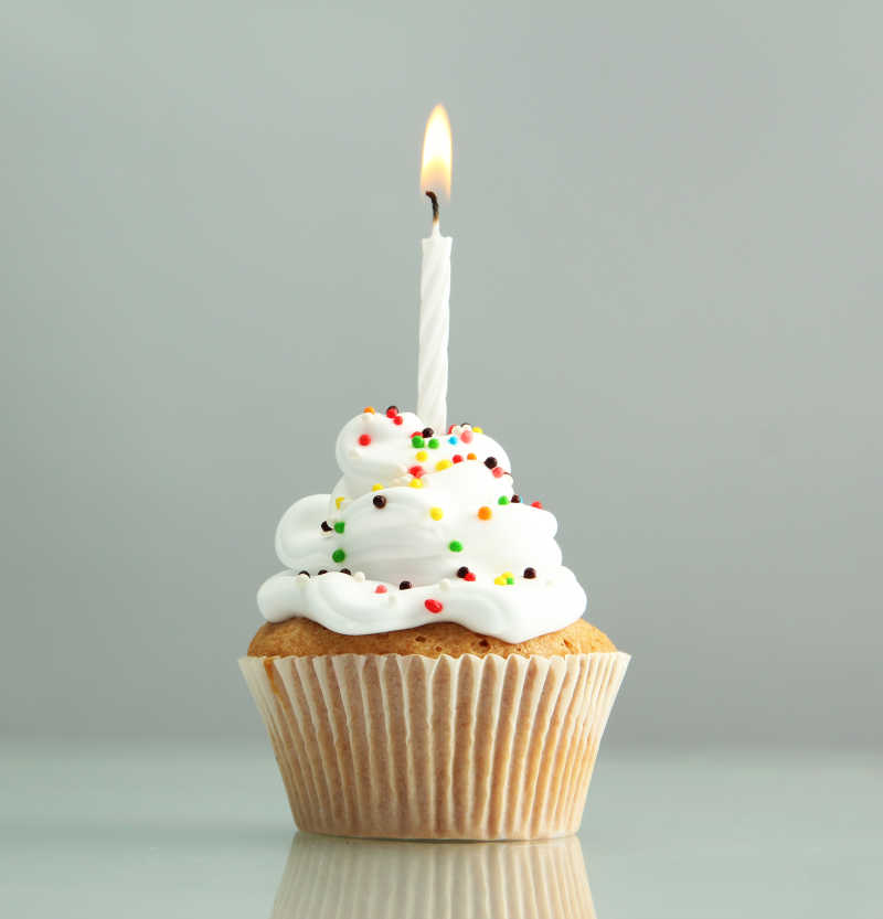 在灰色的背景下的美味的生日蛋糕和蜡烛特写