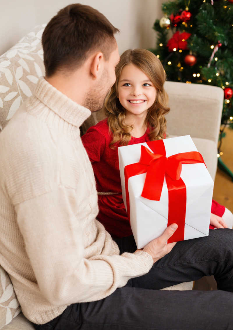 微笑的父亲拿着圣诞礼物看着女儿
