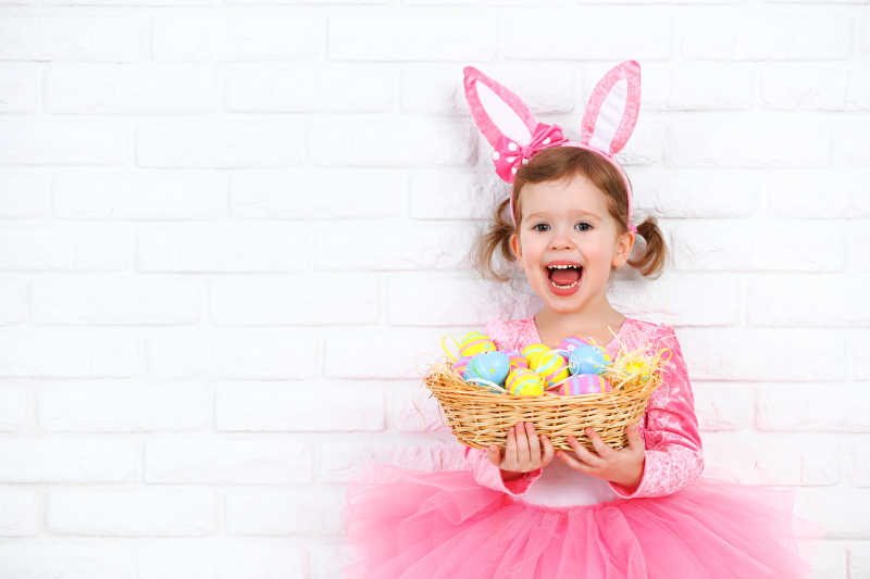 美丽快乐的女孩抱着装复活节彩蛋的篮子