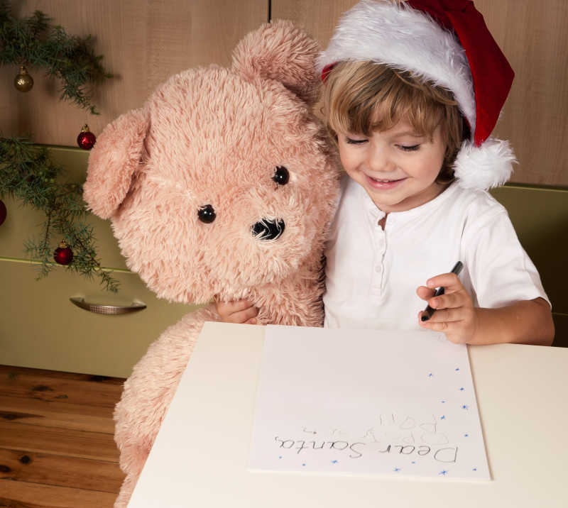 戴着圣诞帽的小女孩抱着泰迪熊写信