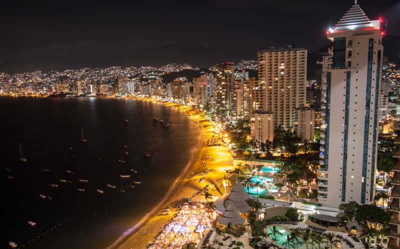 黑色夜空下的假日海滩上灯火通明的城市