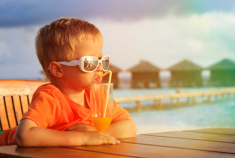 小男孩在热带海滩喝果汁