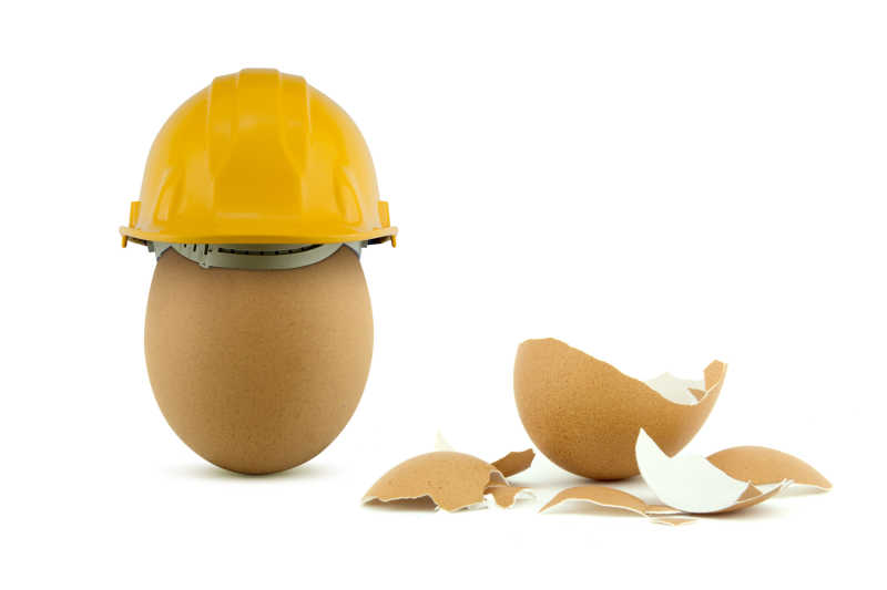 白色背景下鸡蛋的状态提现了安全帽的安全概念