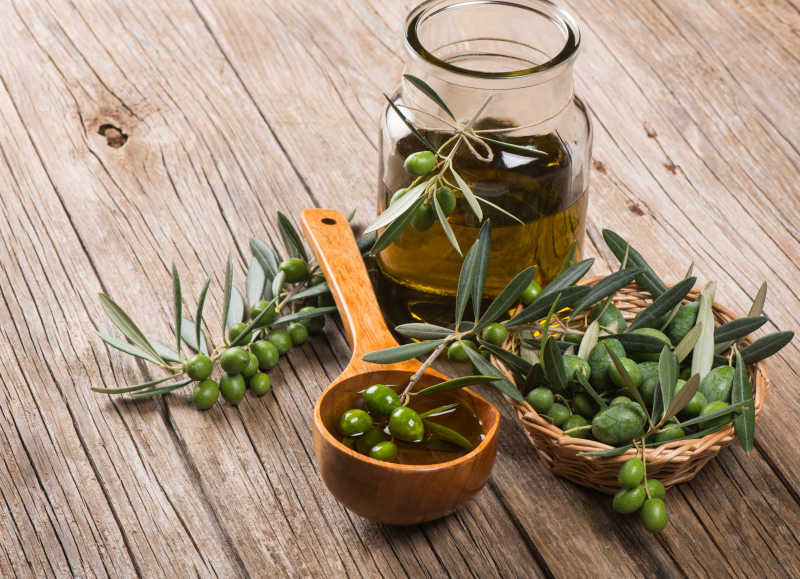 木制桌面上的瓶子里的橄榄油和小木筐里的橄榄果