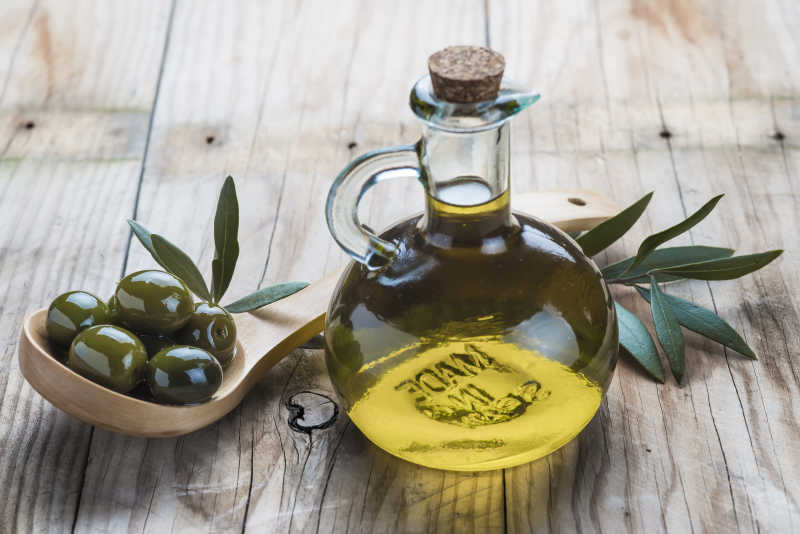 木桌上的一瓶橄榄油和一勺子橄榄果